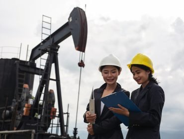 two-female-engineers-stand-beside-working-oil-pumps-with-white-sky